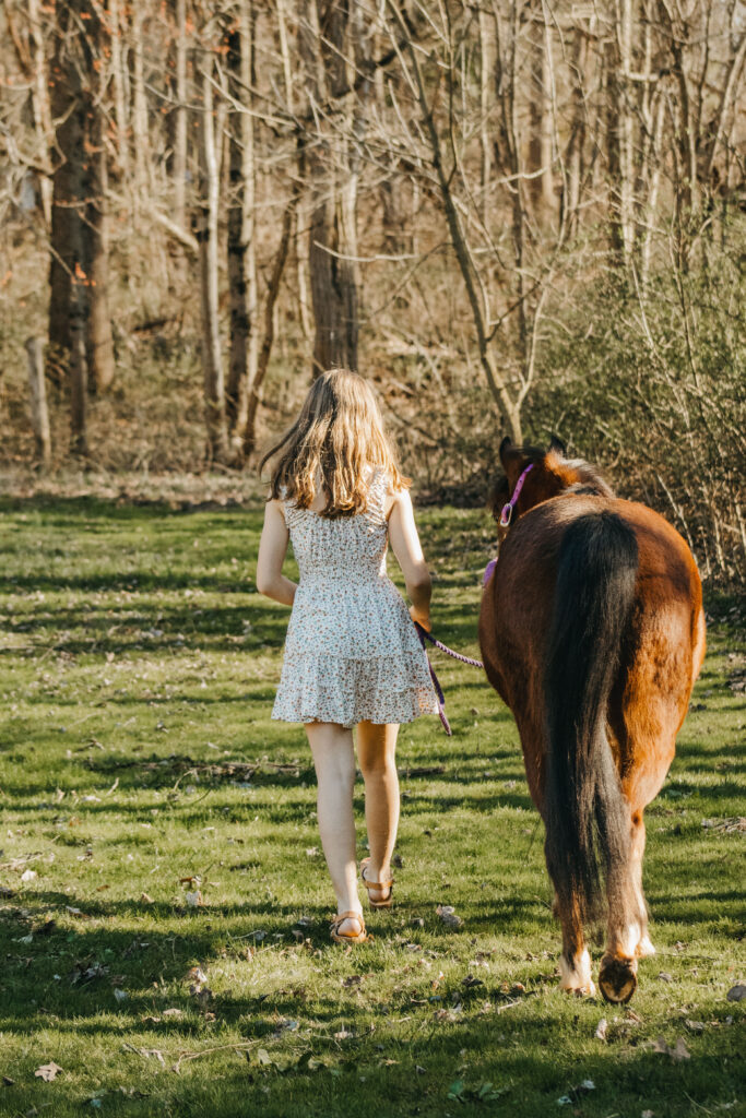 teenage girl leads pony down the path at a horse barn during family photos in the philadelphia suburbs