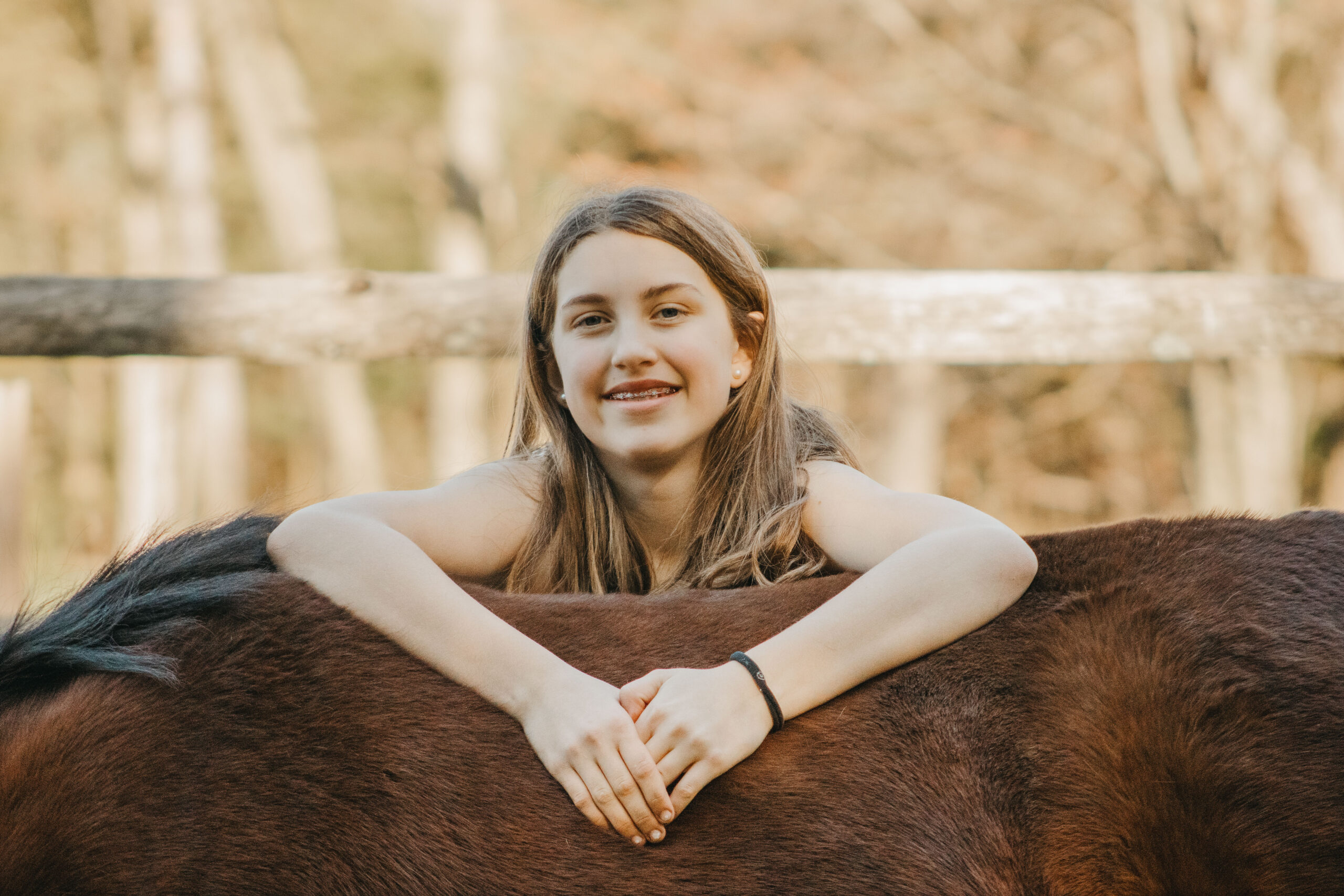 Teen girl smiles while leaning on pony at rustic family photo session in the Philadelphia Region