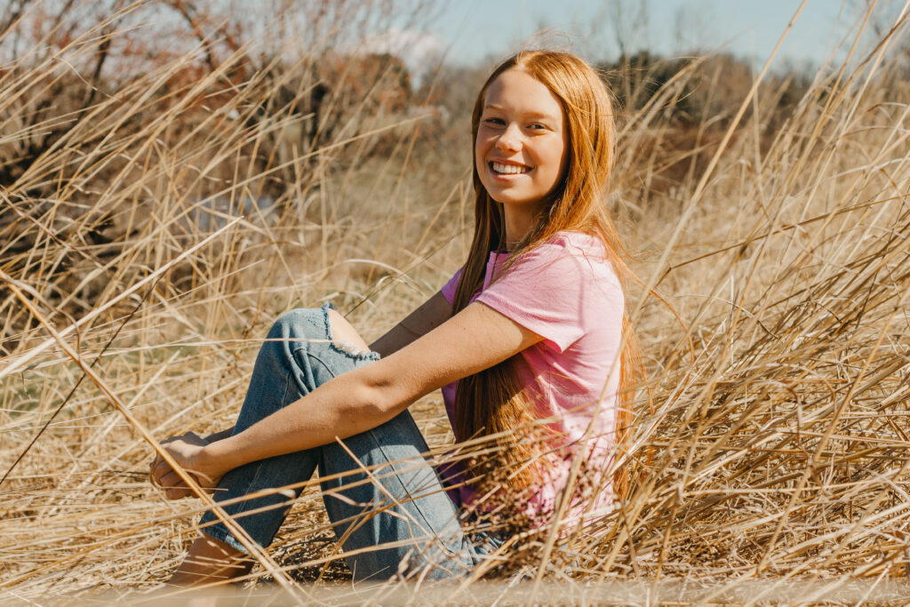 teenager sits in tall grass during mommy and me session in the philadelphia suburbs