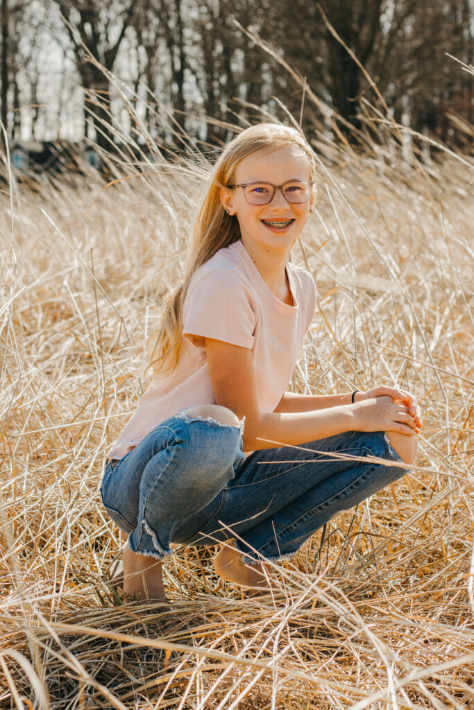 teenage girl kneels in tall grass during Mother Daughter Photoshoot at Marsh Creek State Park in Downingtown, PA