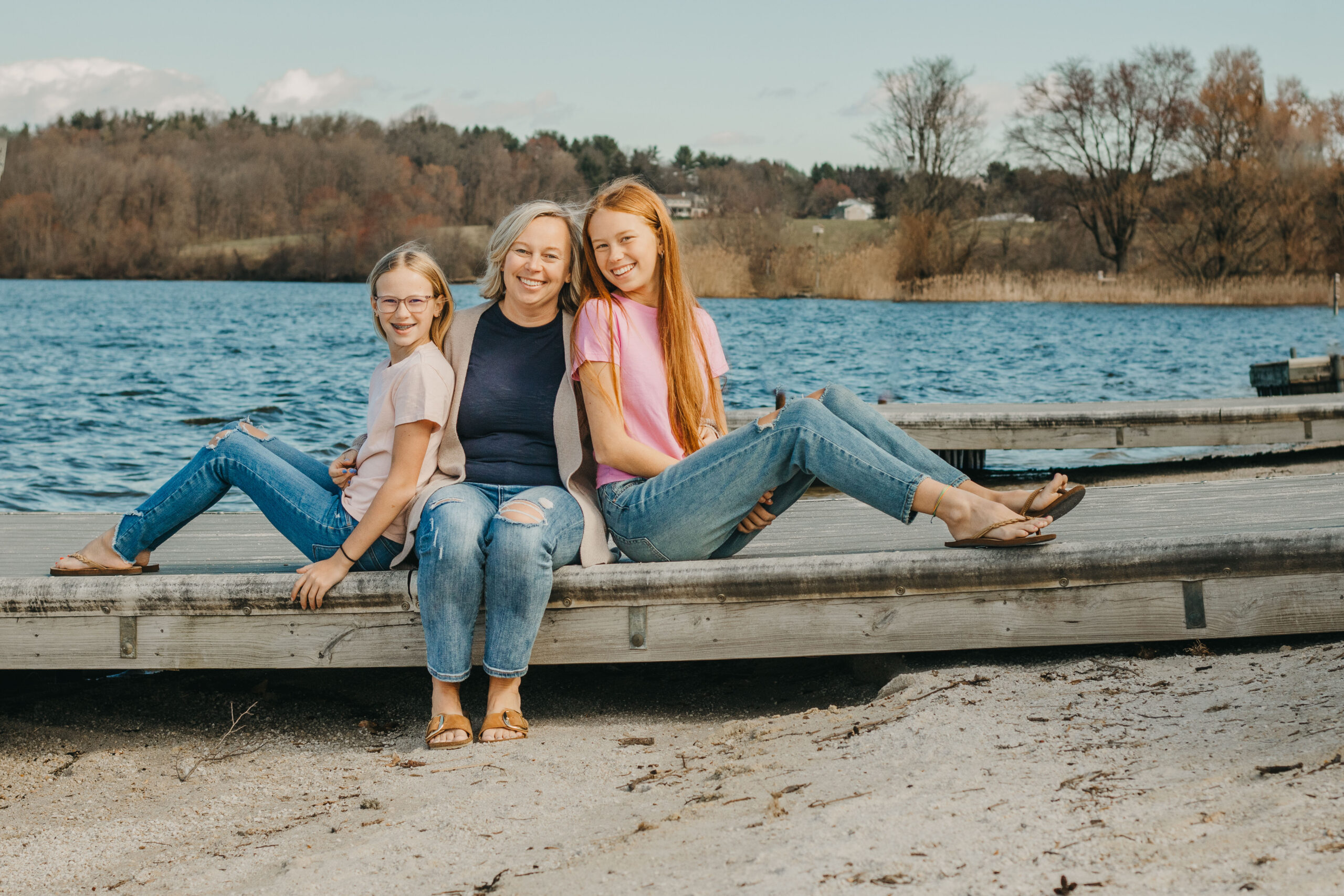 Mother and her 2 teen daughters embrace and smile in front of Marsh Creek State Park during Mommy and Me Session