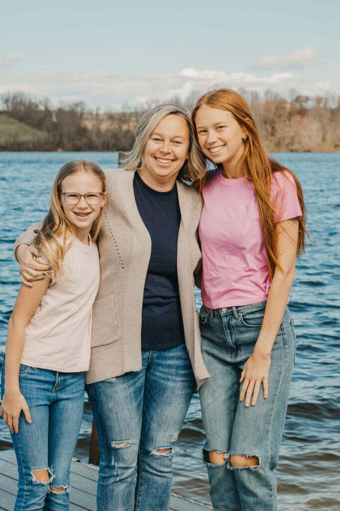 Mother and her 2 teen daughters embrace and smile in front of Marsh Creek State Park during Mommy and Me Session